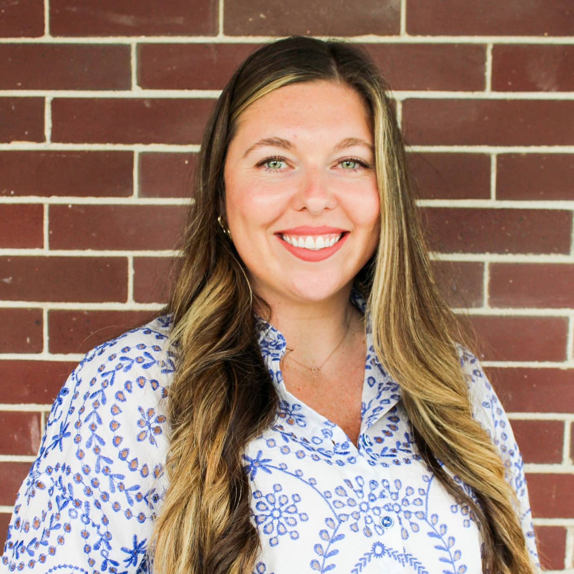 Smiling woman in a white floral blouse standing in front of a brick wall