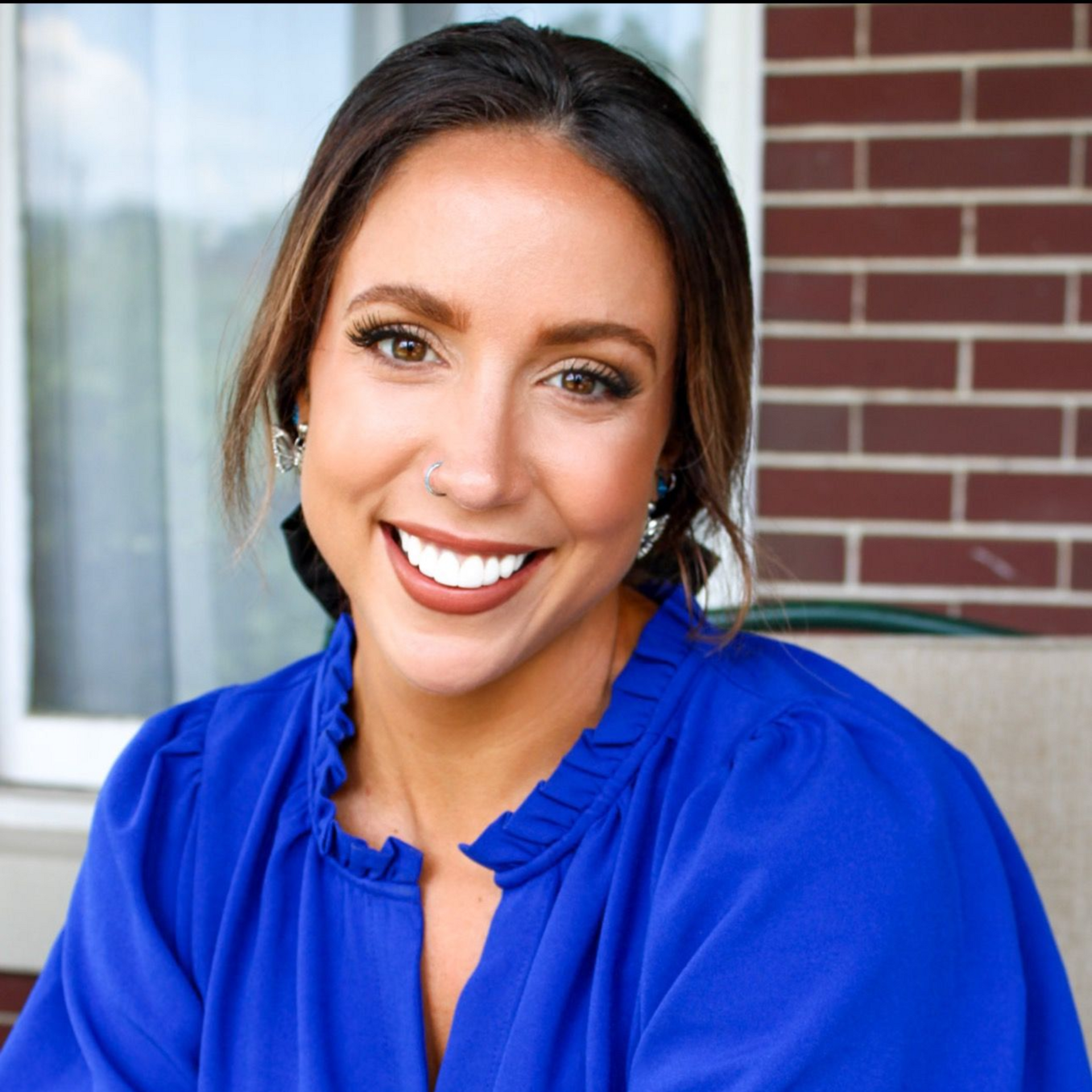 Smiling woman in a bright blue blouse posing outdoors by a brick wall