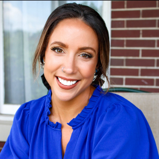 Smiling woman in a bright blue blouse posing outdoors by a brick wall