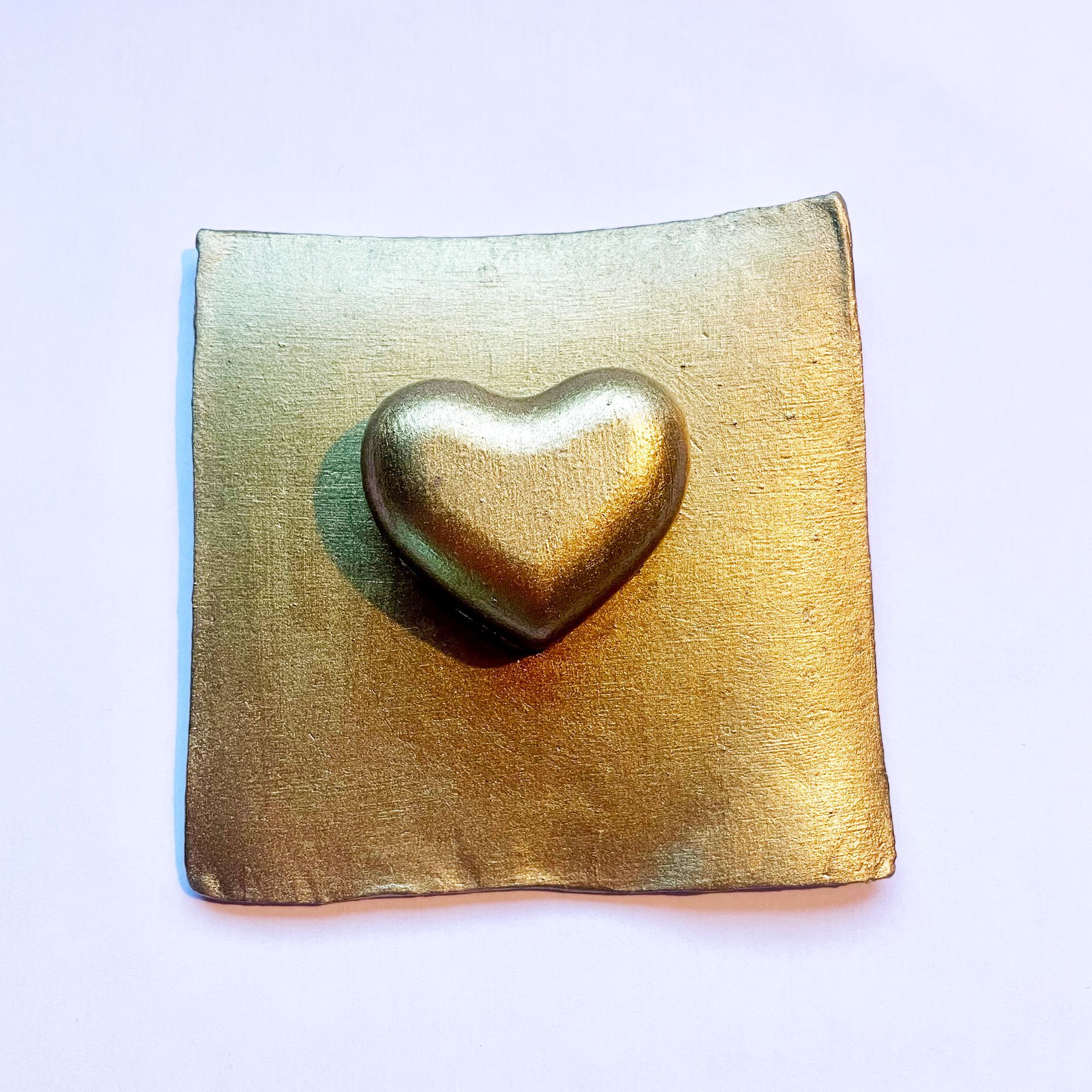 Gouden glitterhartje op een gouden glittervierkantje.