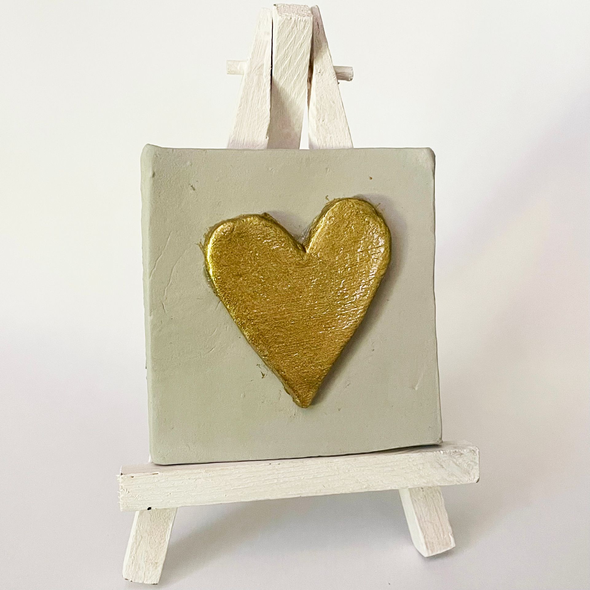 Miniatuurschilderij op ezel: Grijs vierkant met een hartje van gouden glitter. Witte ezel.