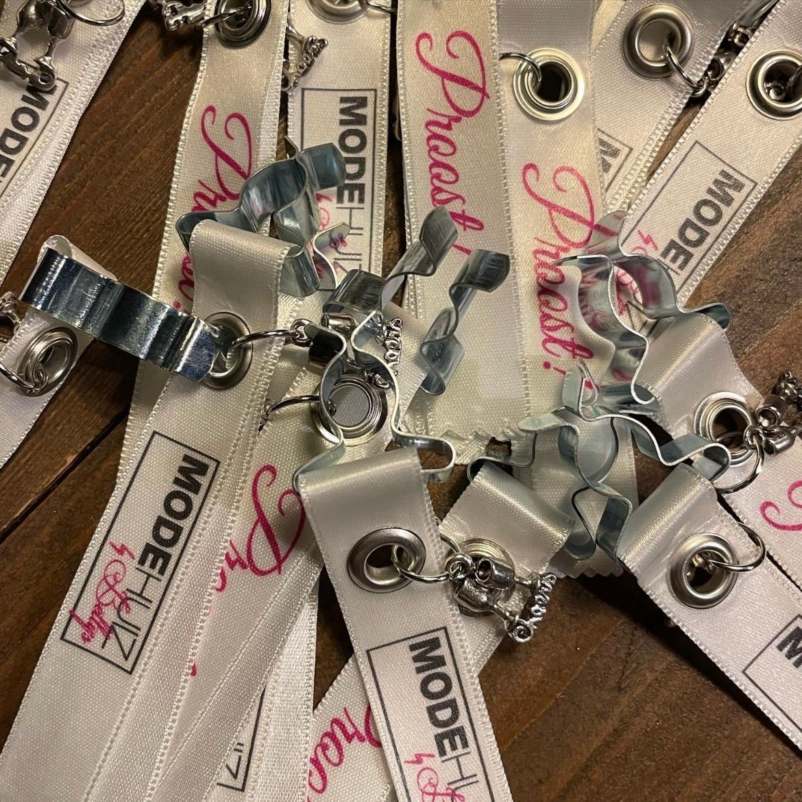  witte linten met metaalkleurige klemmetjes. Op de linten staat in roze letters modehuis bij betty's
