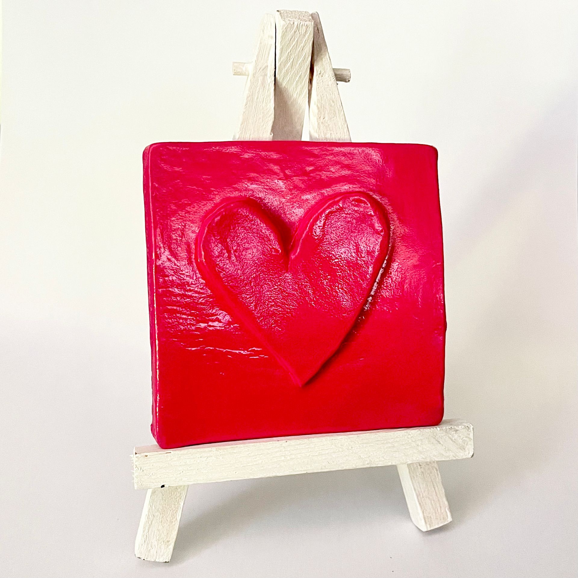 Rood vierkant kunstwerk met hartreliëf, op een miniatuur witte schildersezel.