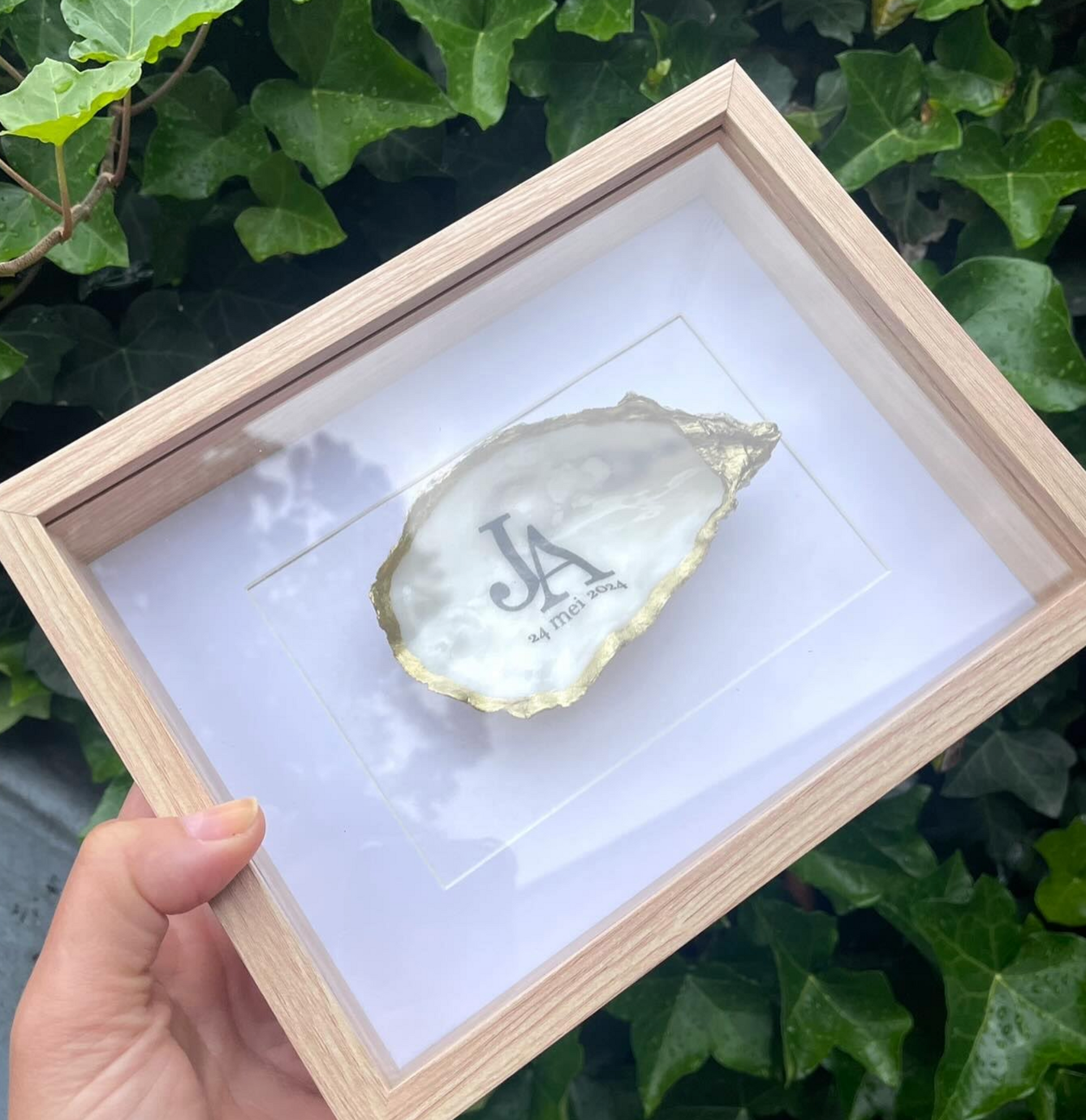 Een vitrinekastje met een ingelijste, vergulde oesterschelp met initialen.