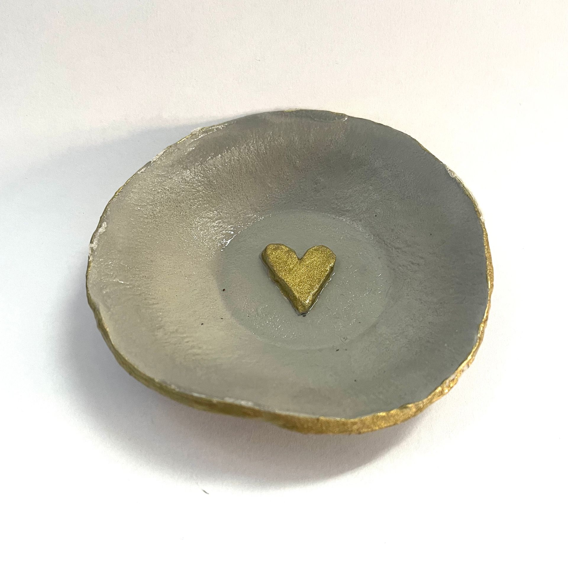 Grijze, ronde keramische schaal met een goudkleurig glitterhartje in het midden en een gouden rand.