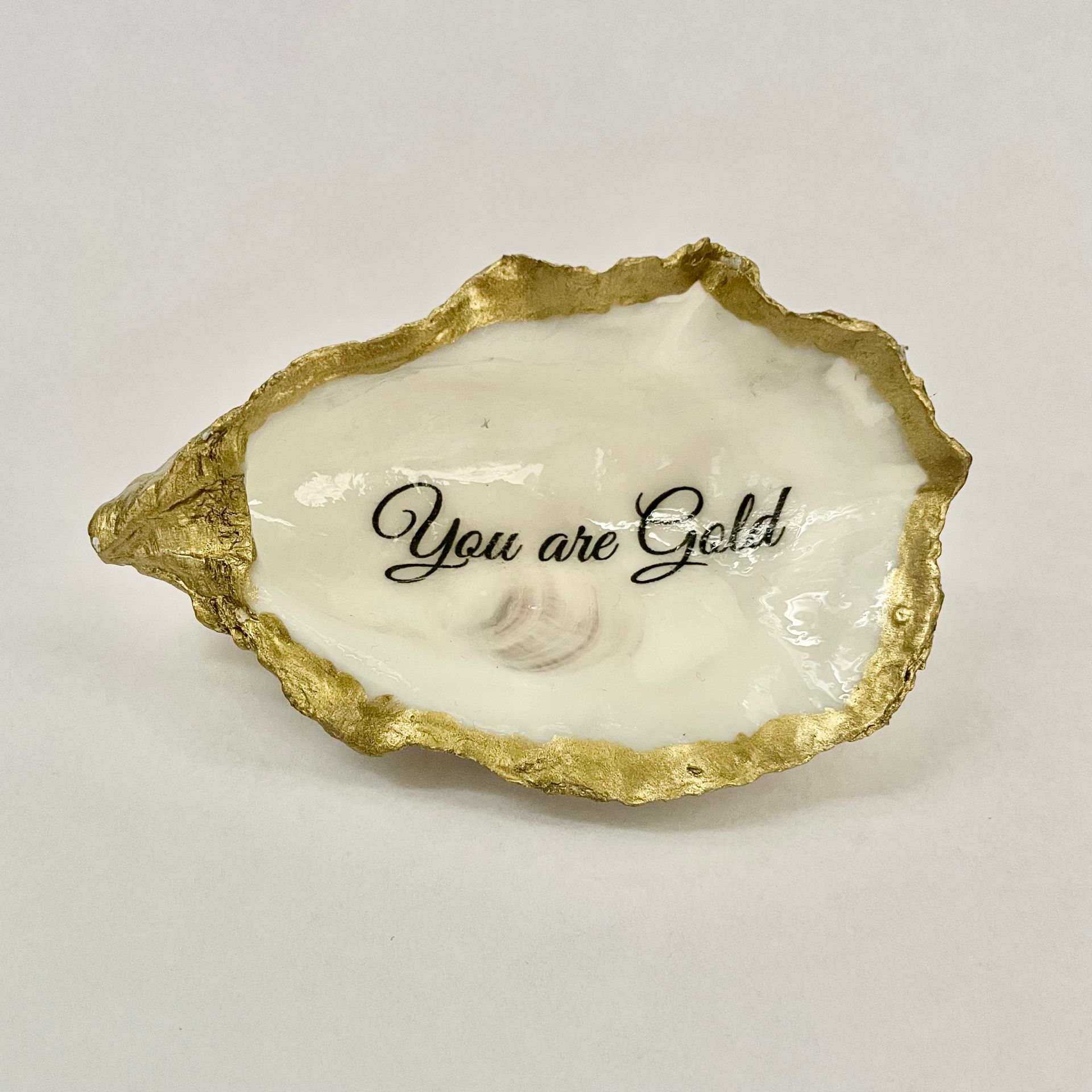 Een met goud beschilderd sieradenschaaltje in de vorm van een oesterschelp met de tekst You are gold