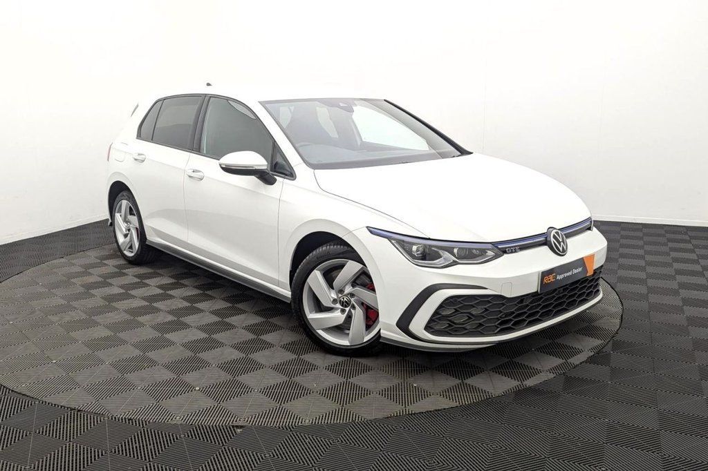 White hatchback car photographed in a studio, front-left view on a patterned floor.