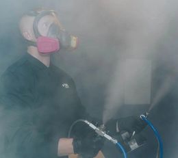 Person in a respirator spraying a mist in a smoky industrial setting