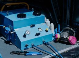 Blue industrial machine with gauges, hoses, and tools in a dark workspace