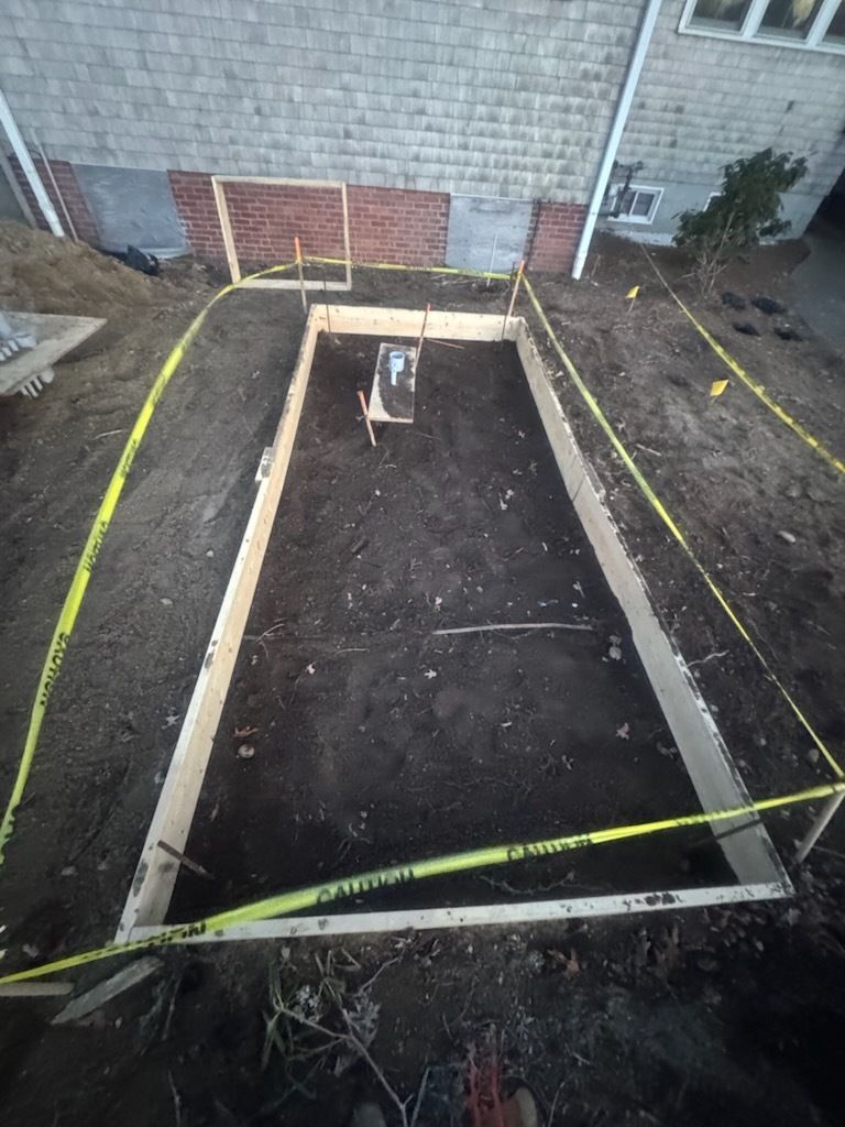 Backyard excavation framed by wooden forms, with yellow caution tape around a rectangular pit.