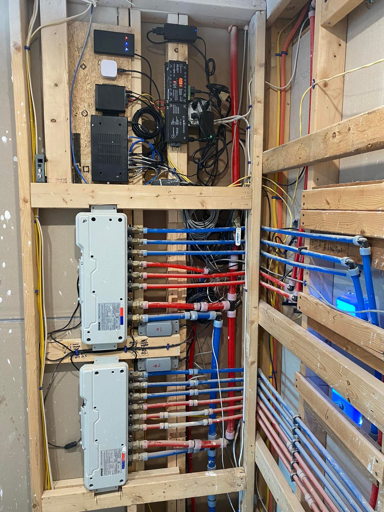 Open electrical panel with blue and red wiring inside a wooden wall cavity