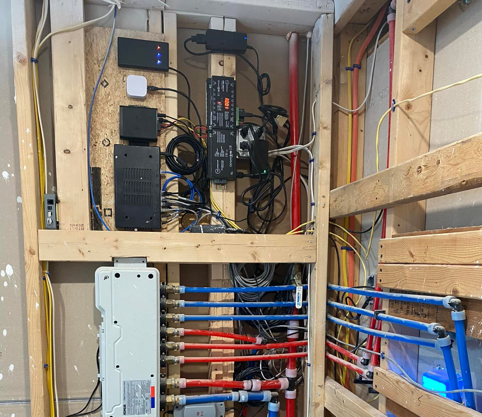 Open electrical and network wiring panels inside a wooden utility wall, with cables and blue pipes.
