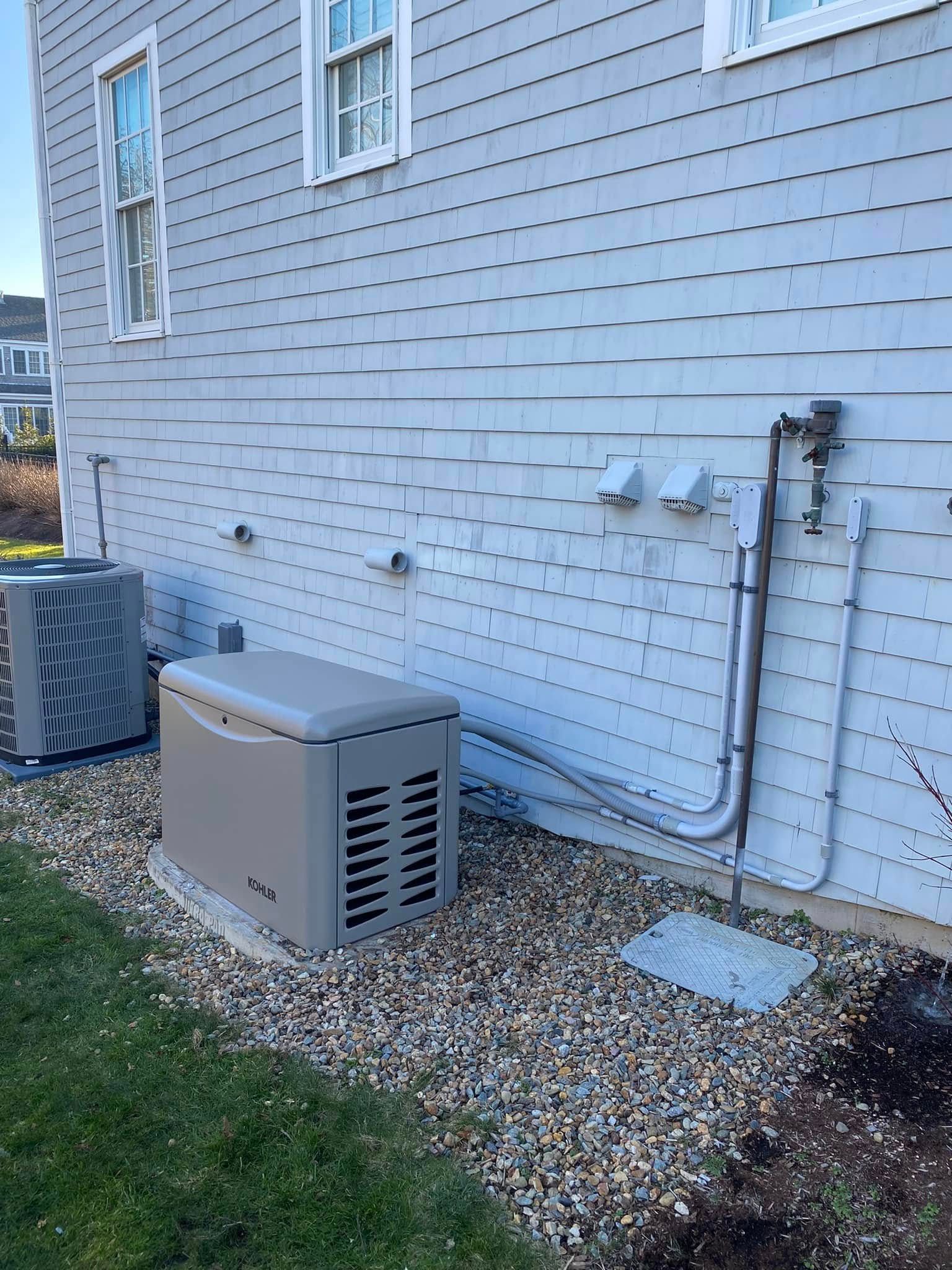 Outdoor HVAC unit beside a white house wall with utility meters and pipes over a gravel strip