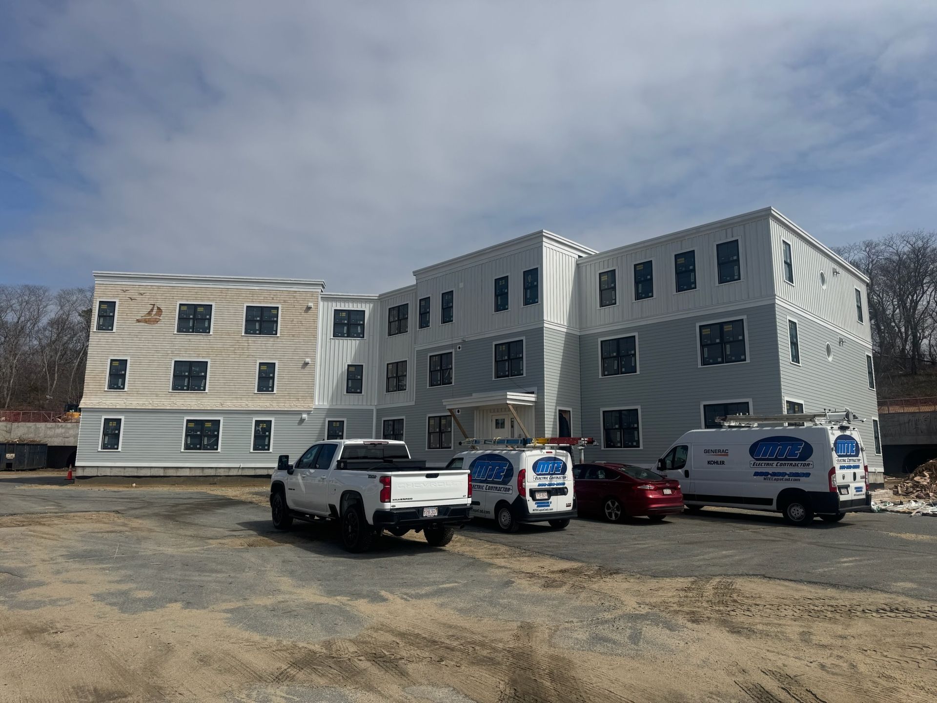 Three-story office building with parked trucks and vans on a gravel lot under a clear sky