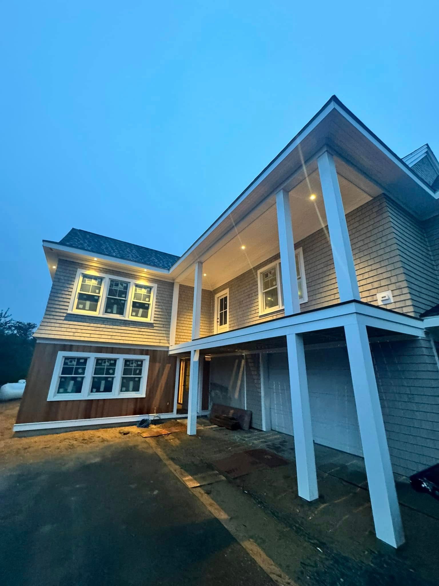 Large white two-story house with lit windows and a covered porch at dusk