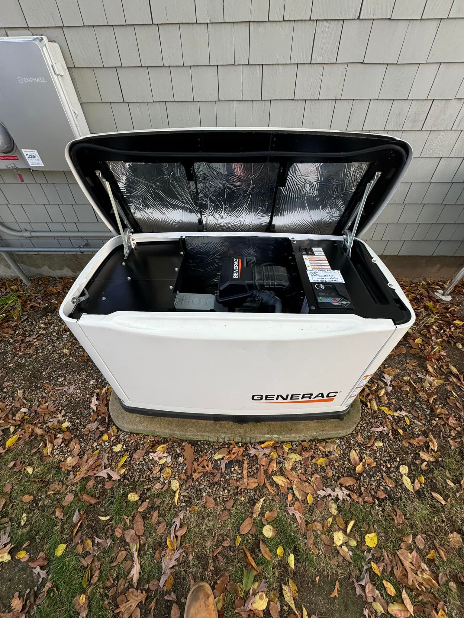 Open white utility bin with black lid by a house wall, containing a black bag and small items.