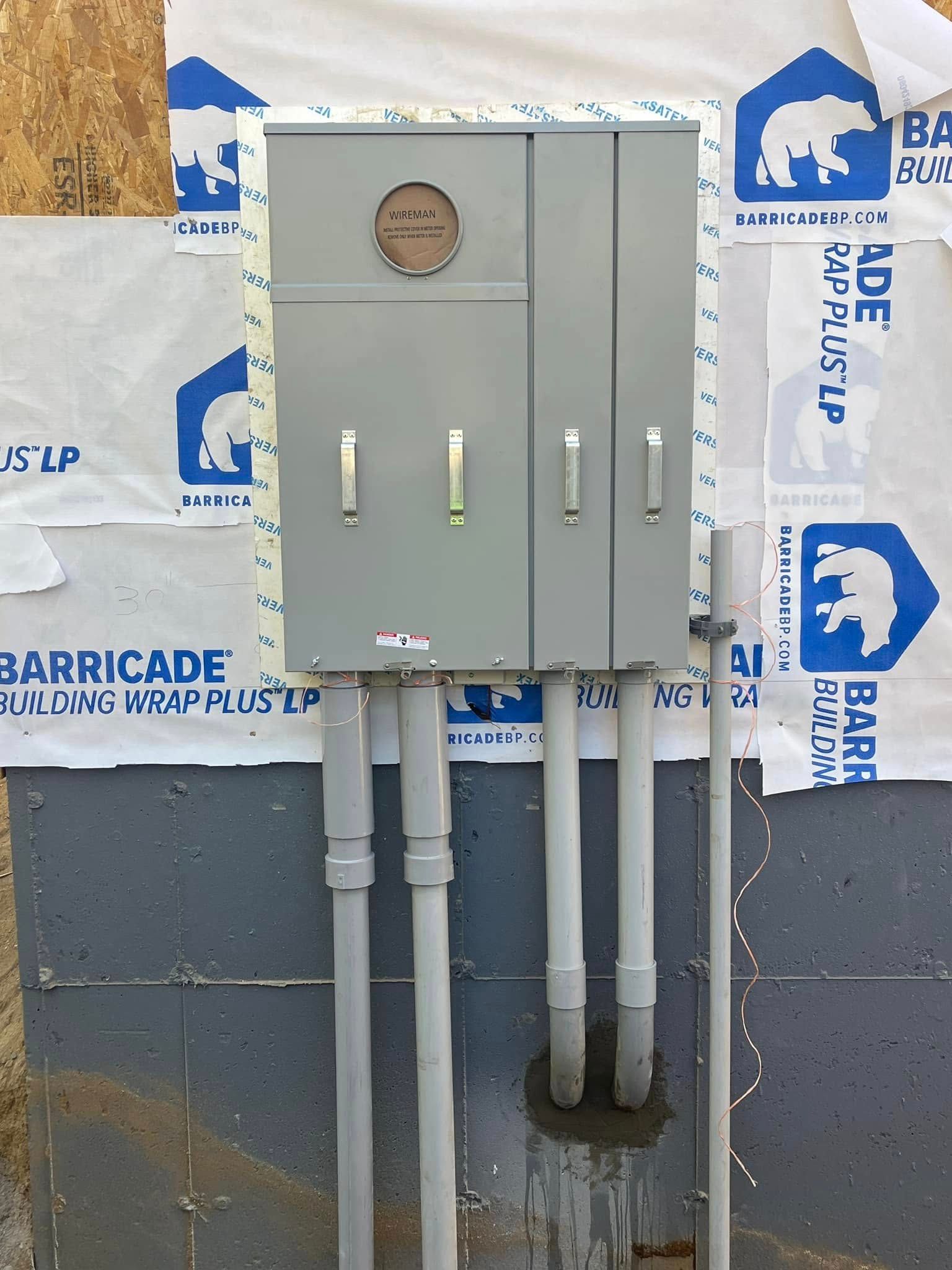 Gray electrical utility boxes and conduit mounted on a wall with Barricade wrap in the background
