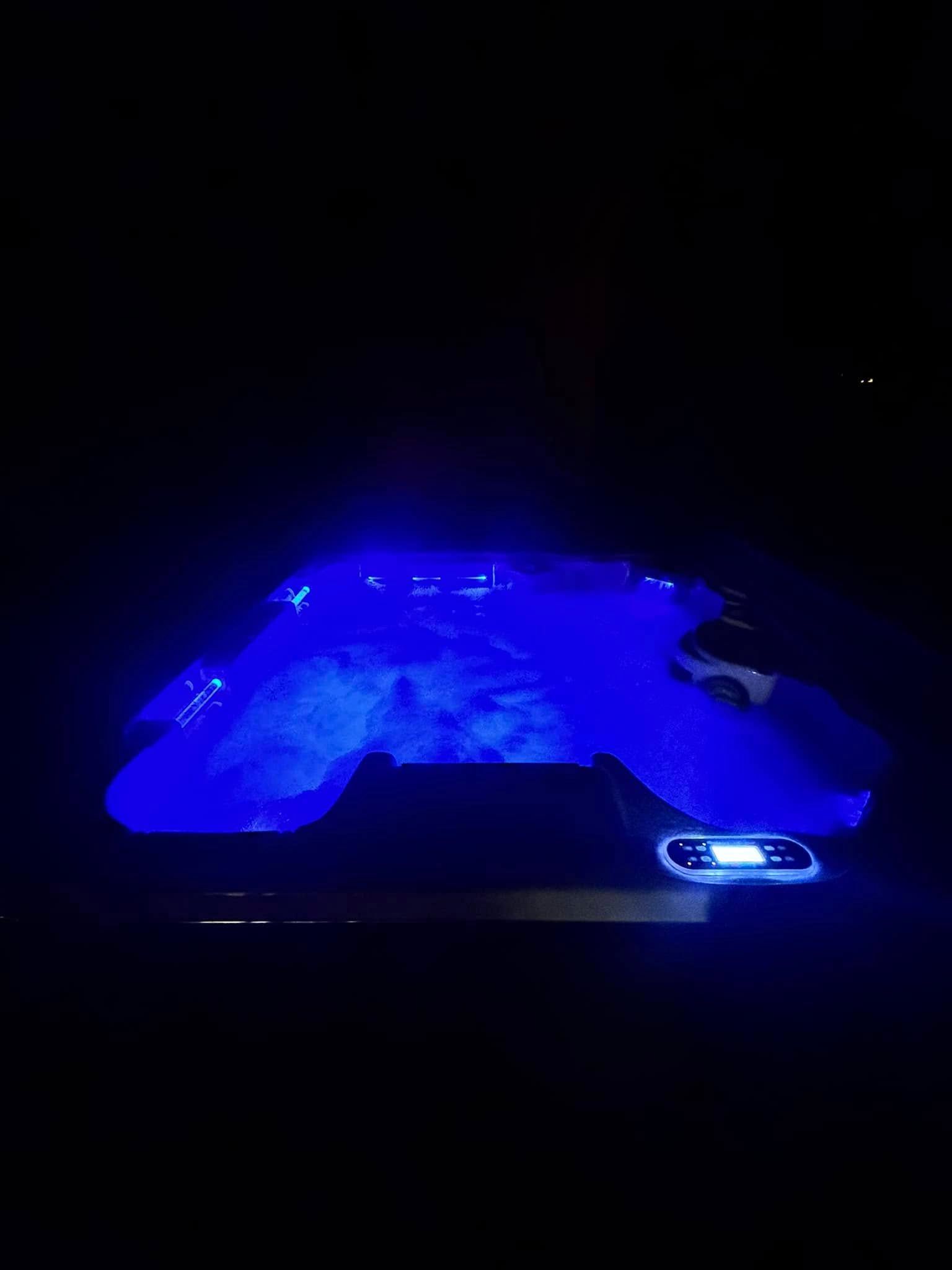 Blue-lit hot tub in a dark room, with a covered edge and a phone on the side.