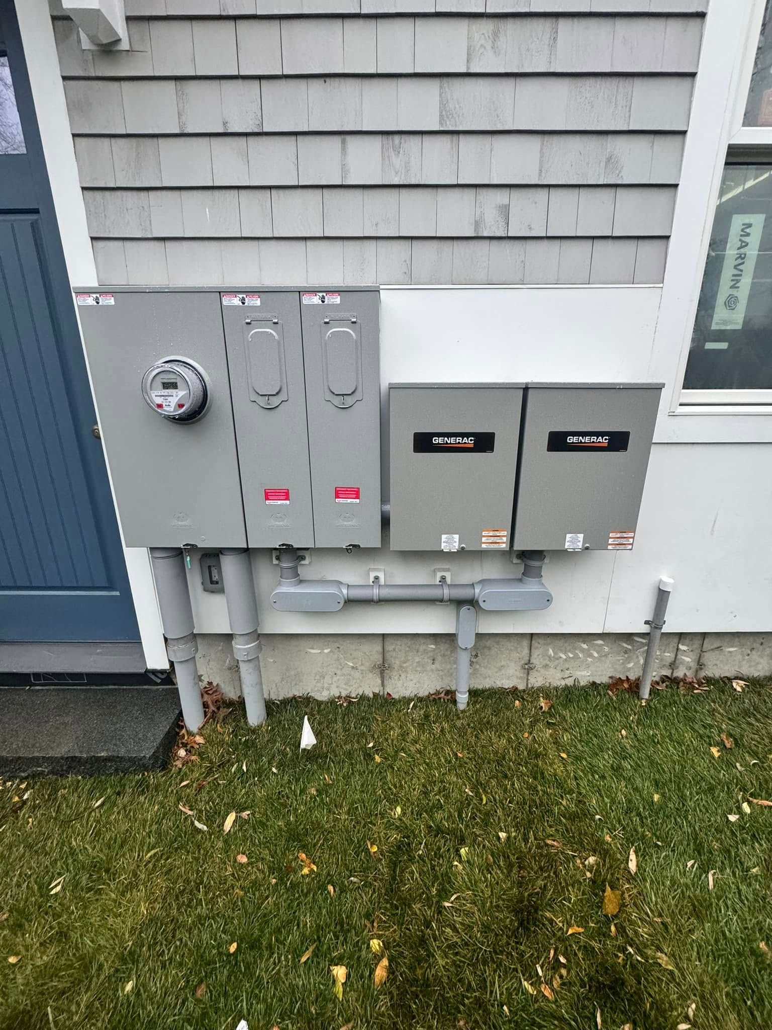 Gray utility meters and electrical boxes mounted on the outside of a house above grass.