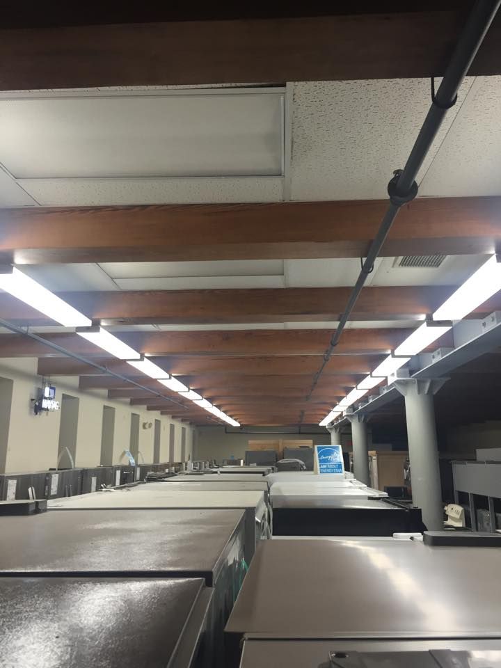 Warehouse interior with rows of metal bins under fluorescent lights and exposed ceiling beams