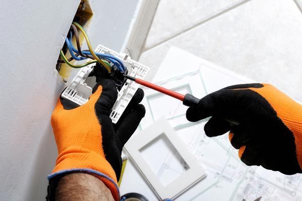 Electrician’s gloved hands wiring a ceiling fixture with a screwdriver.