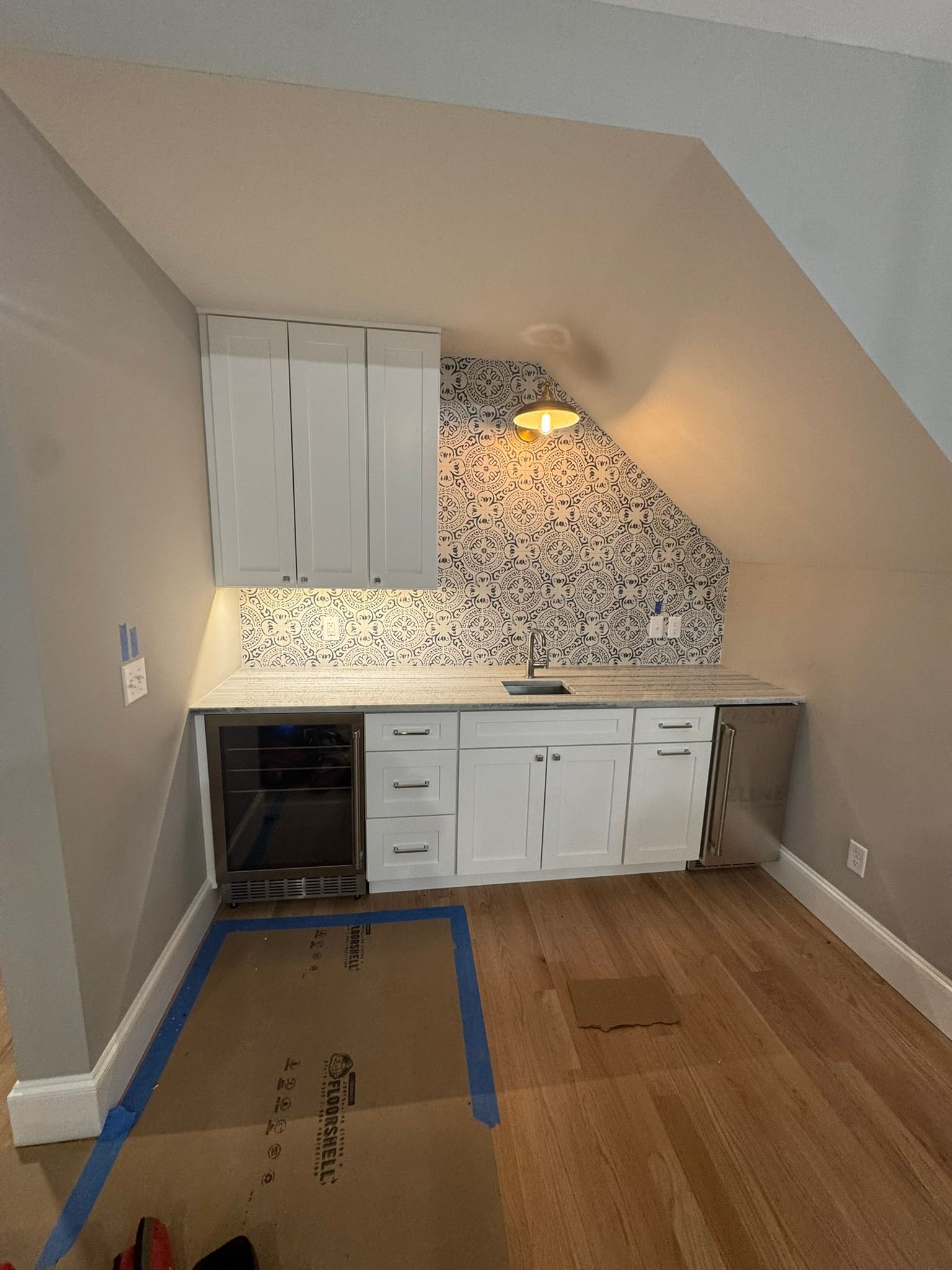 Small attic kitchenette with white cabinets, mosaic backsplash, and a warm wall light.