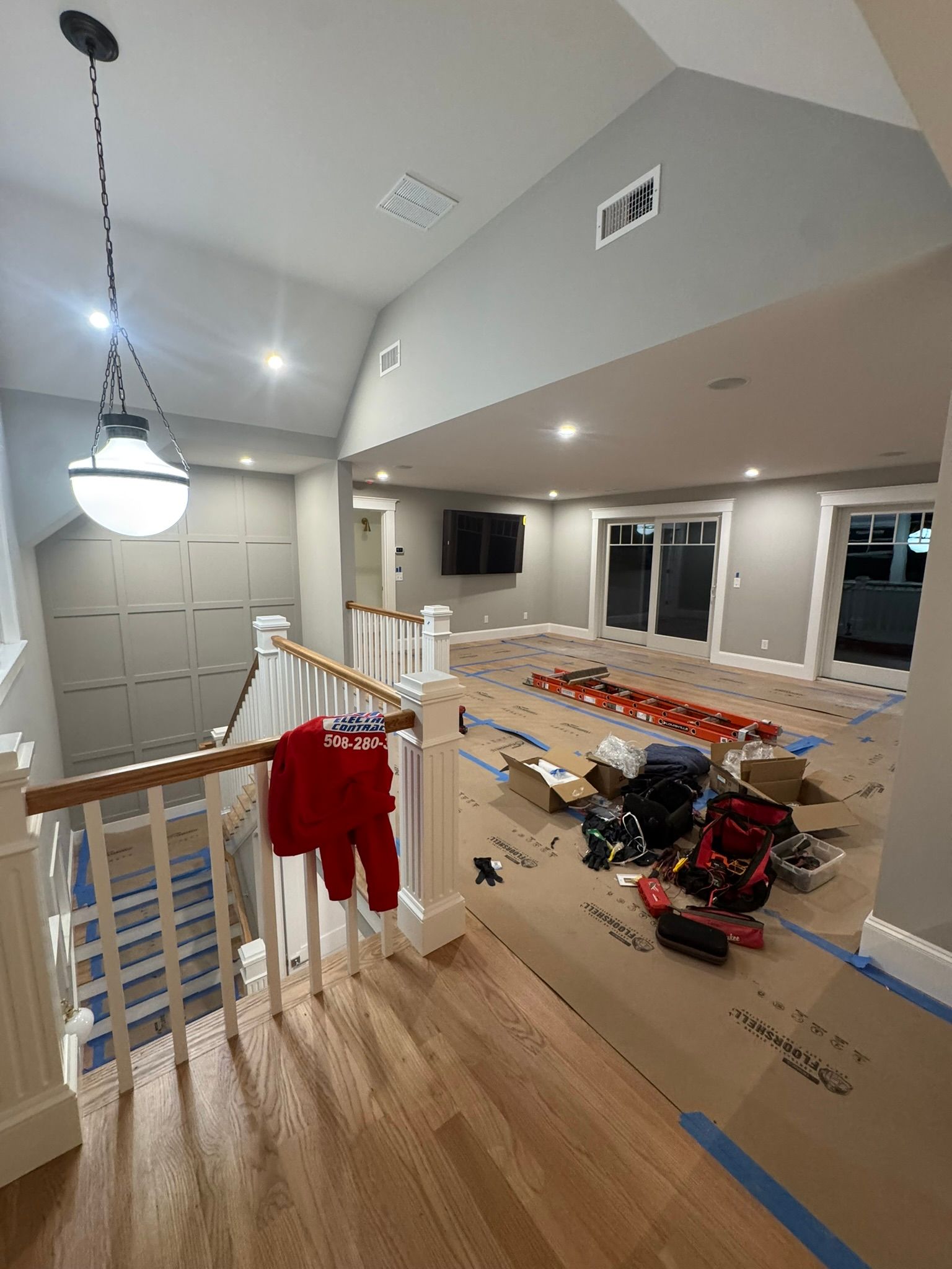 Stair landing under construction with red tool bags, taped flooring, and hanging light fixture in a bright home