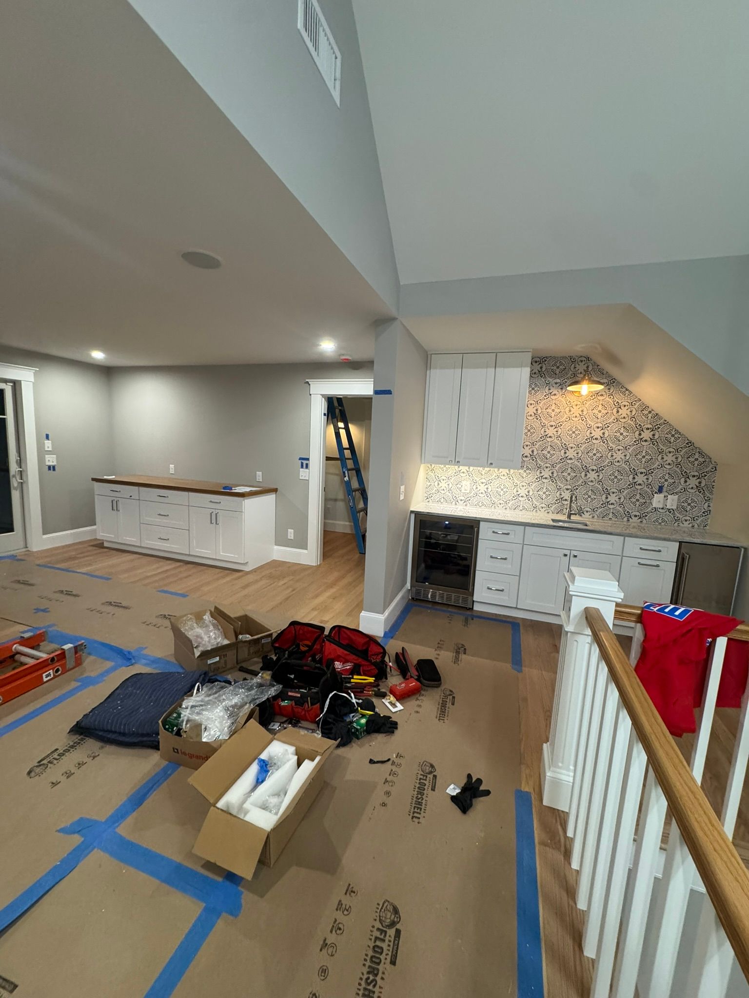 Messy upstairs room with tools, boxes, and debris on covered floor beside a kitchen area
