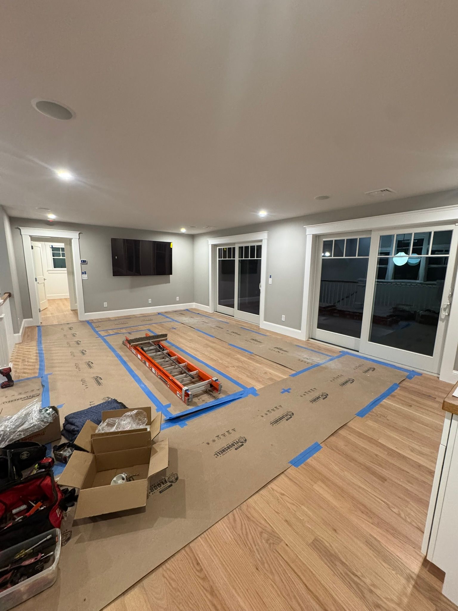 Living room under renovation with flooring covered in protective paper, tools, and exposed underlayment