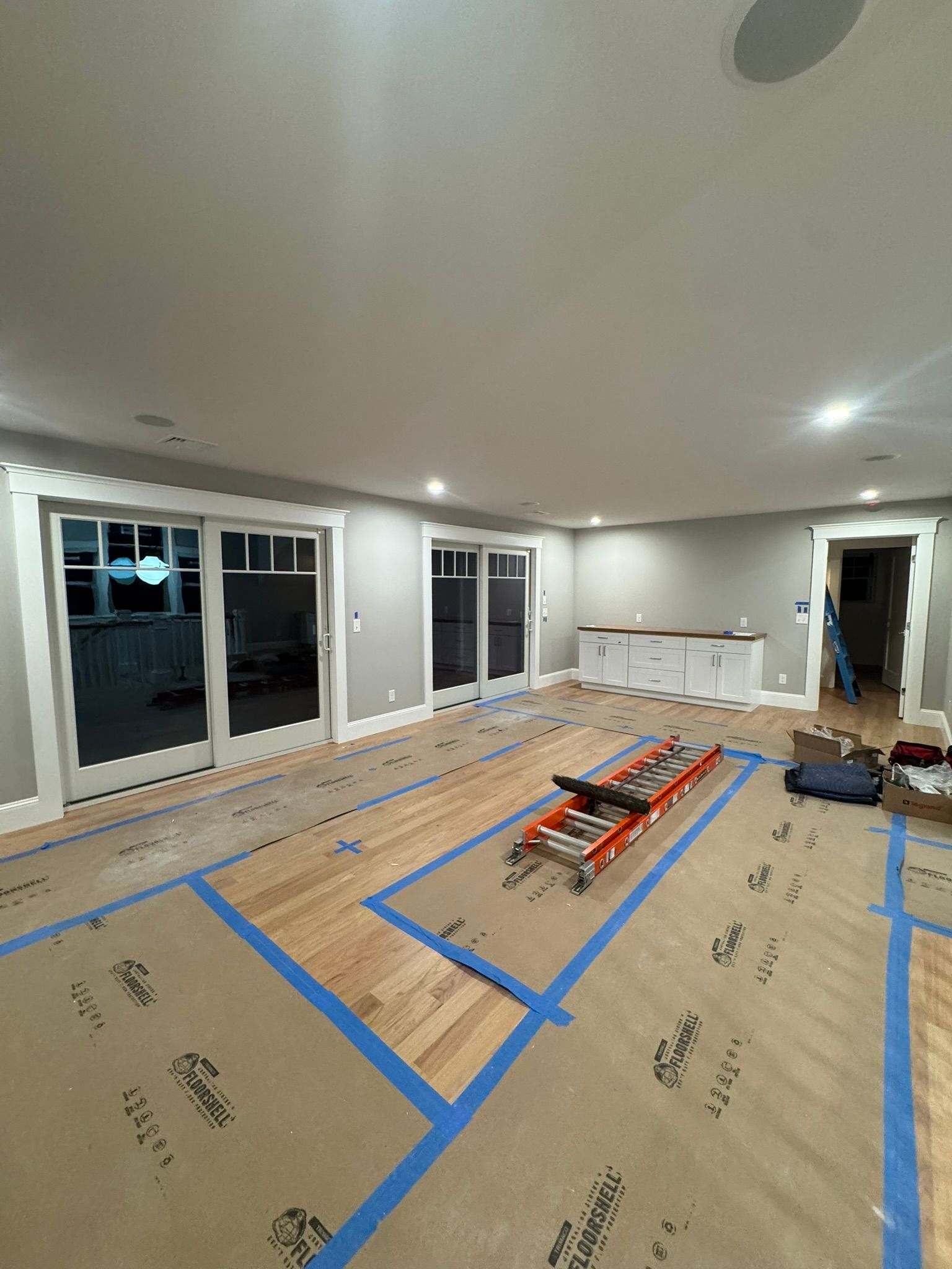 Empty living room under renovation with blue painter’s tape, tools, and stacked materials on the floor