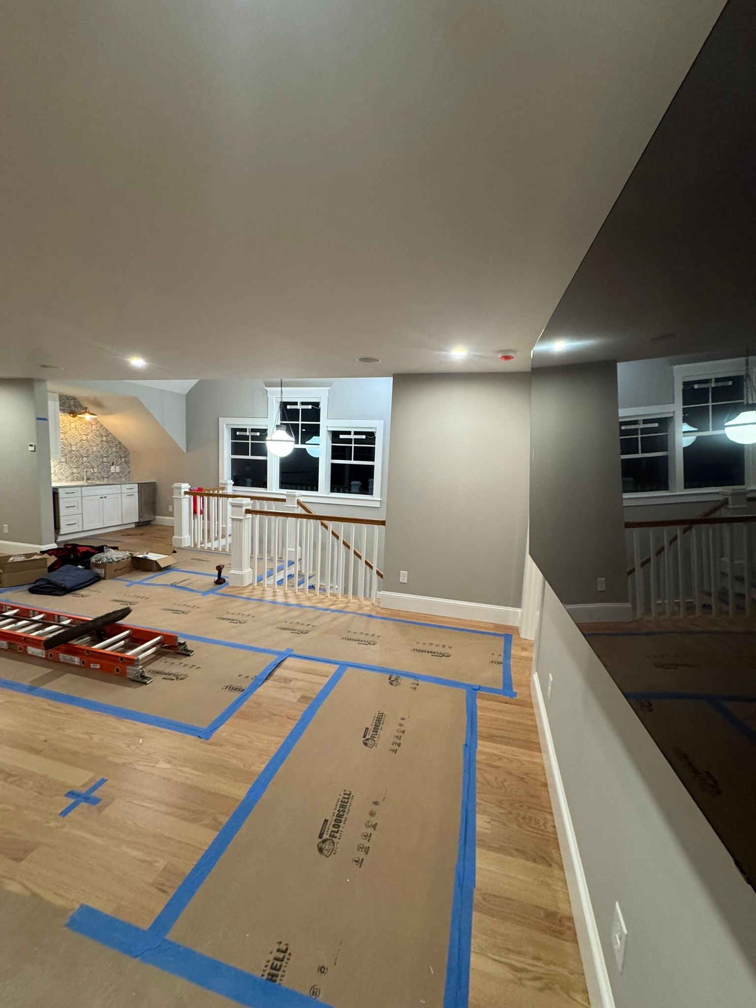 Renovated room with blue-taped floor protection, exposed materials, and windows overlooking a dark exterior.