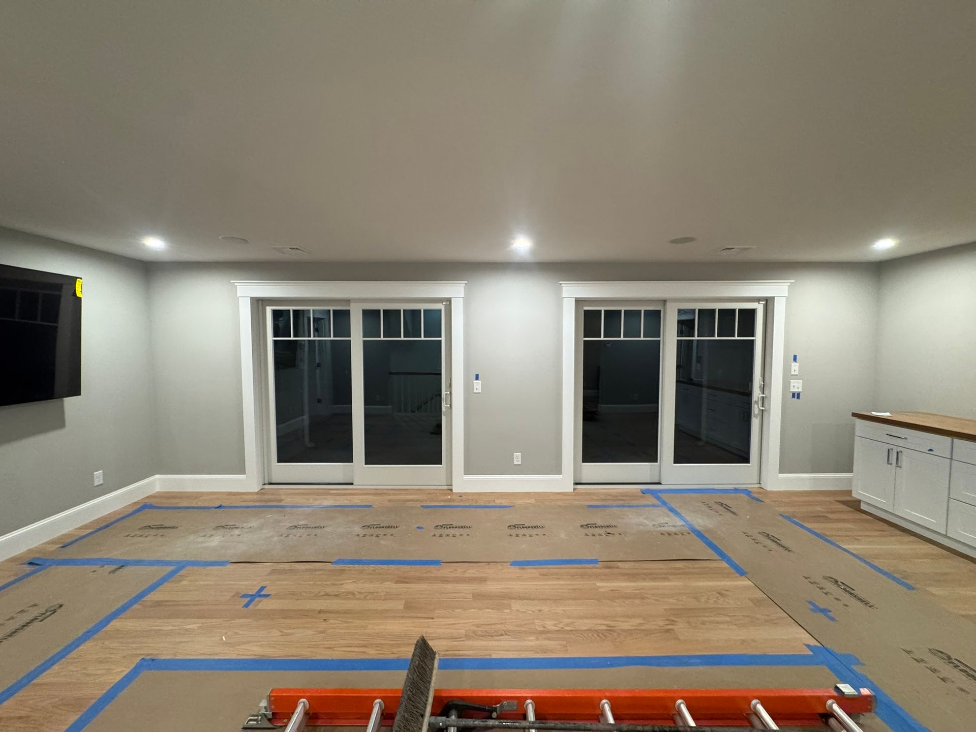 Empty living room with taped-off floor layout, recessed lights, sliding glass doors, and a wall-mounted TV.
