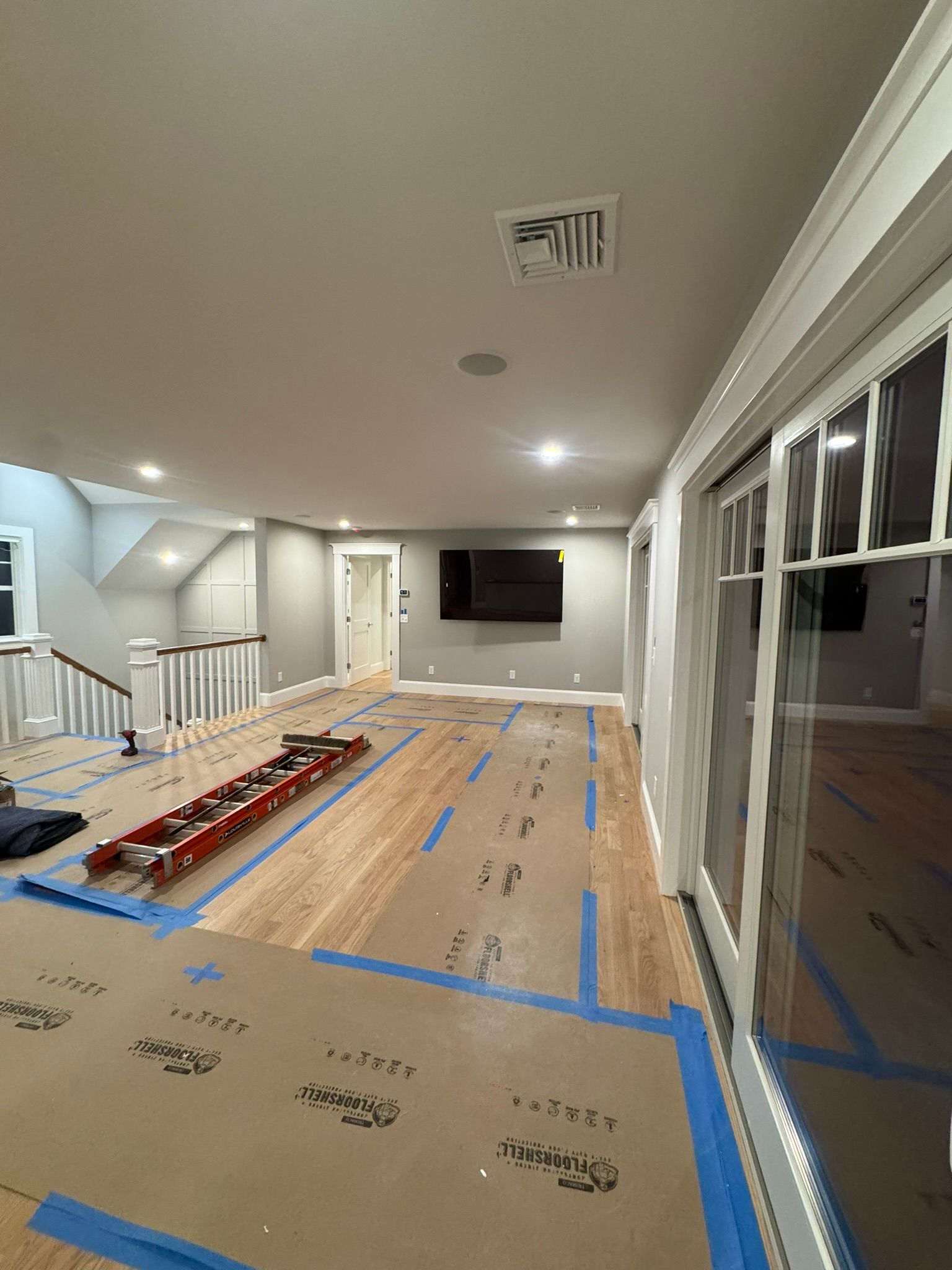 Renovated living room with hardwood floor, blue tape lines, recessed lights, and wall-mounted TV