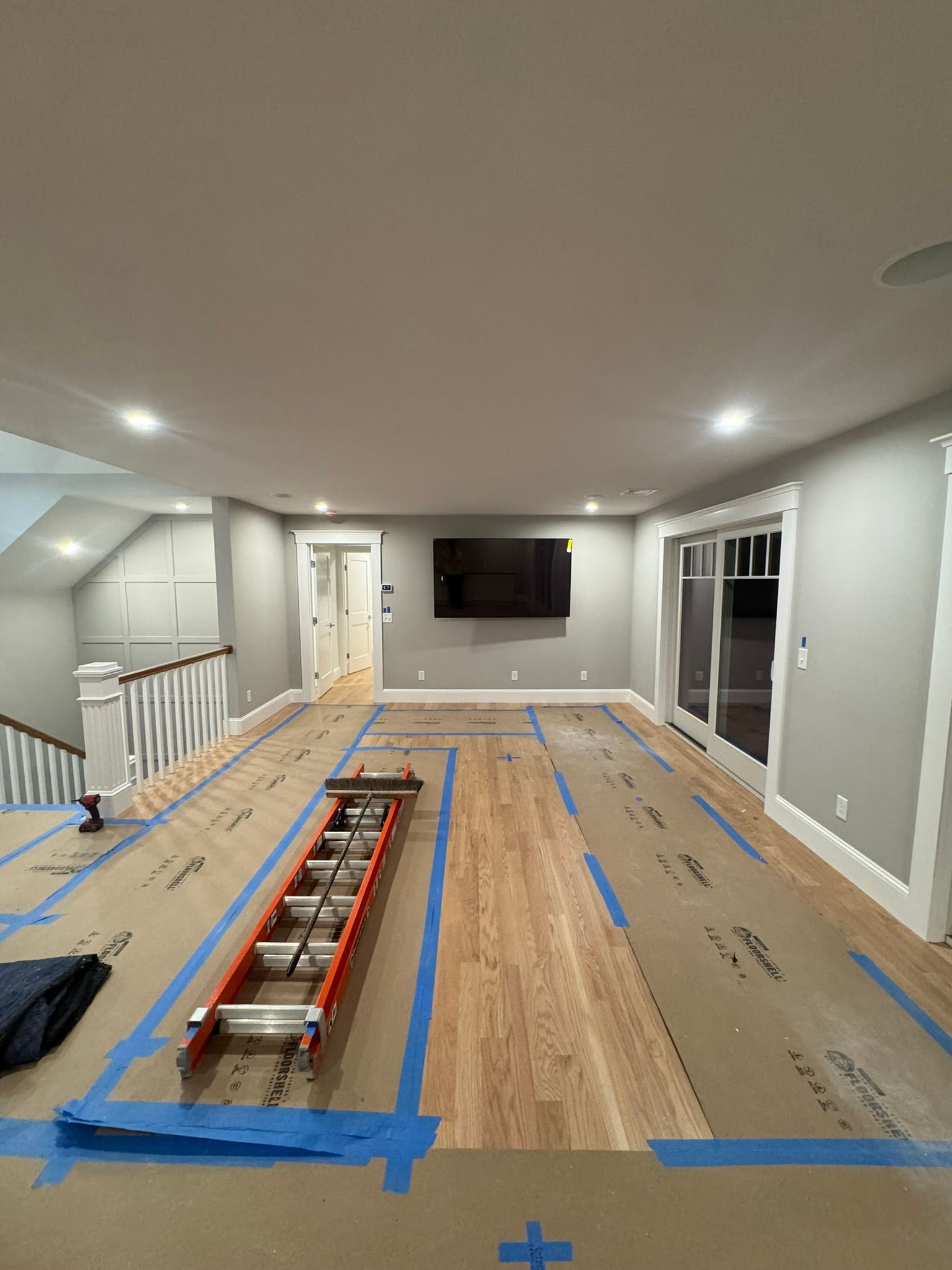 Renovation room with taped flooring, ladder, and wall-mounted TV under recessed lights