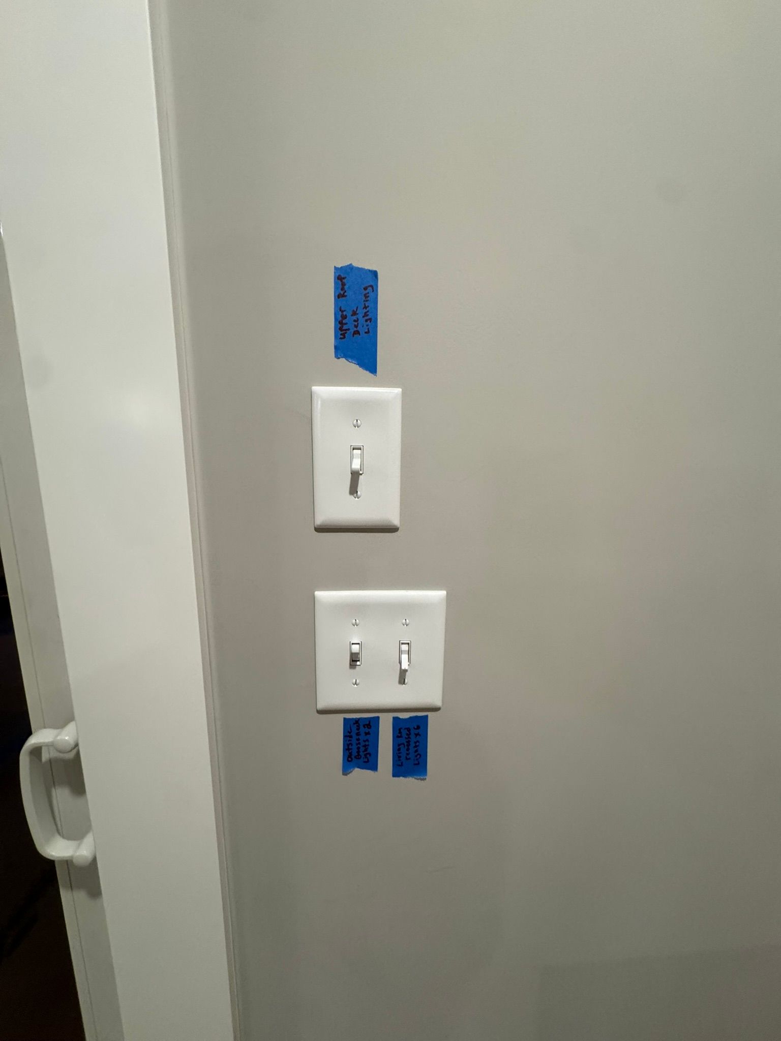 Wall with two white light switches and blue painter’s tape labels above and below them