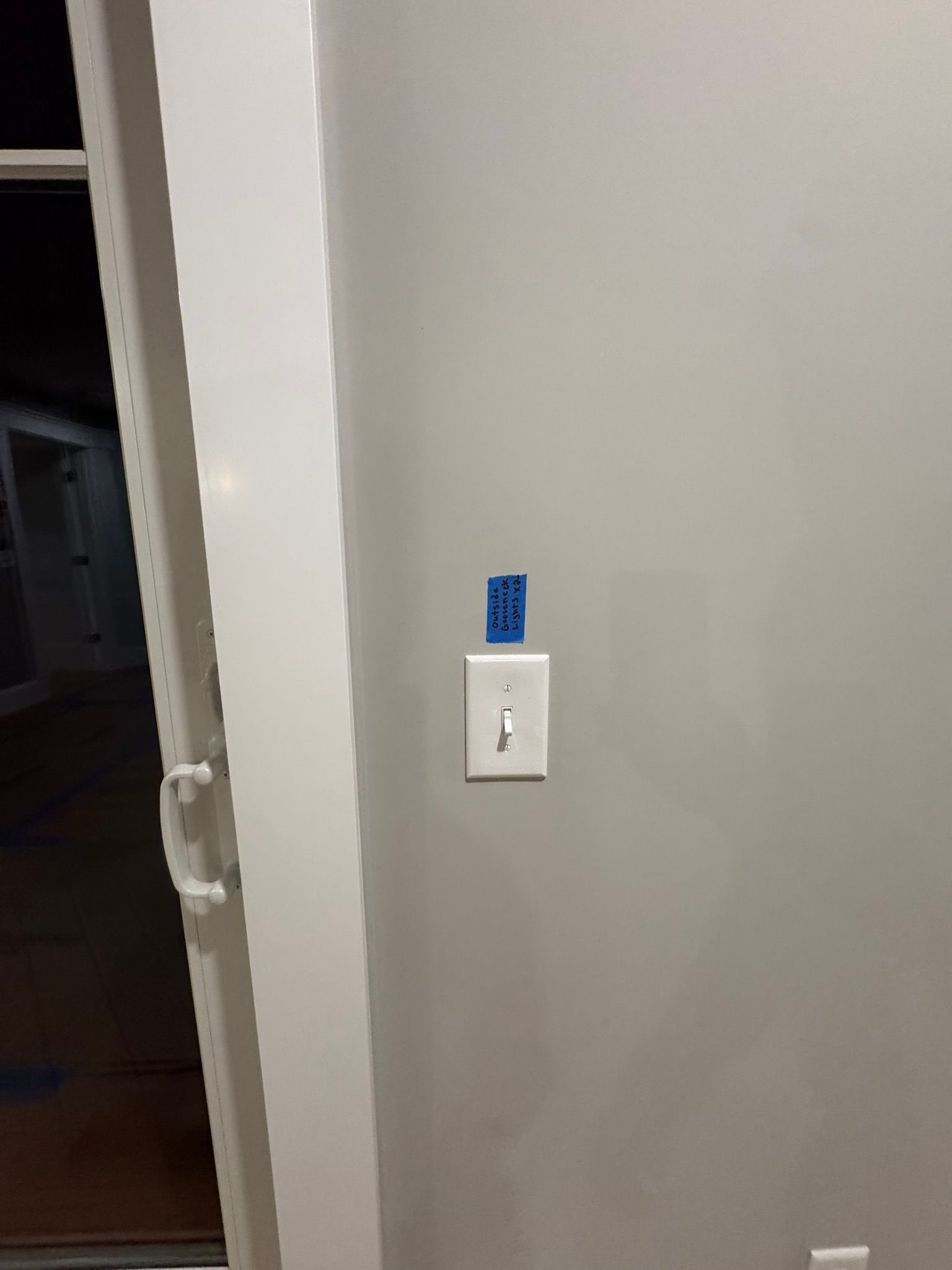 White wall with a light switch and blue label beside an open doorway.