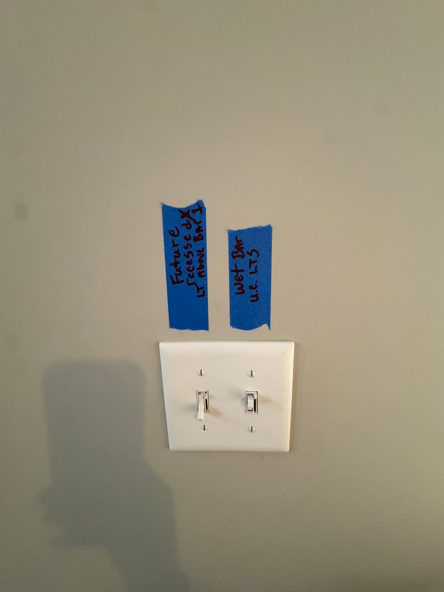 Wall with a white light switch and two blue tape labels above it.