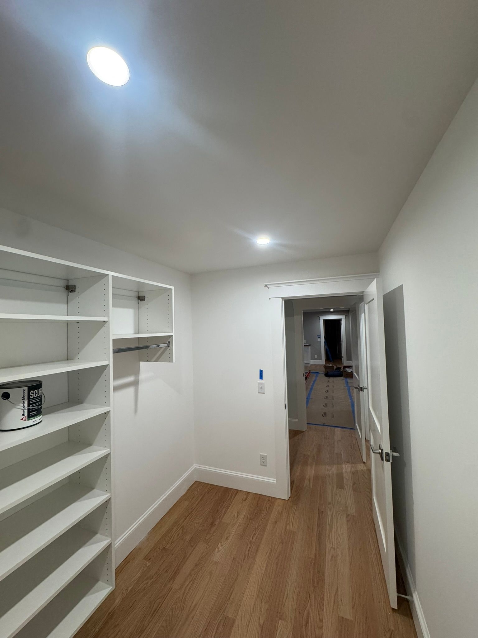 Narrow white hallway with built-in shelves, wood floor, and recessed ceiling lights.
