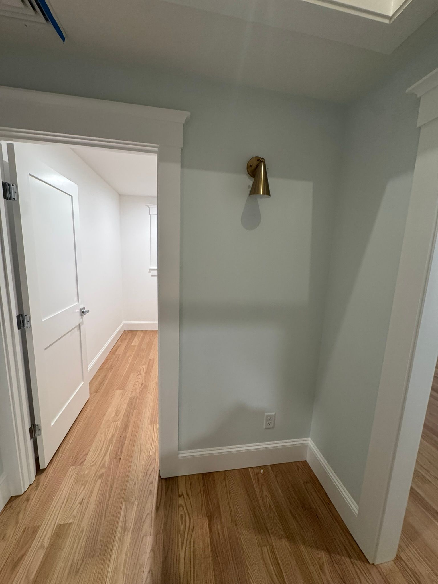 Empty hallway nook with gray walls, wood floor, white trim, and a small wall light