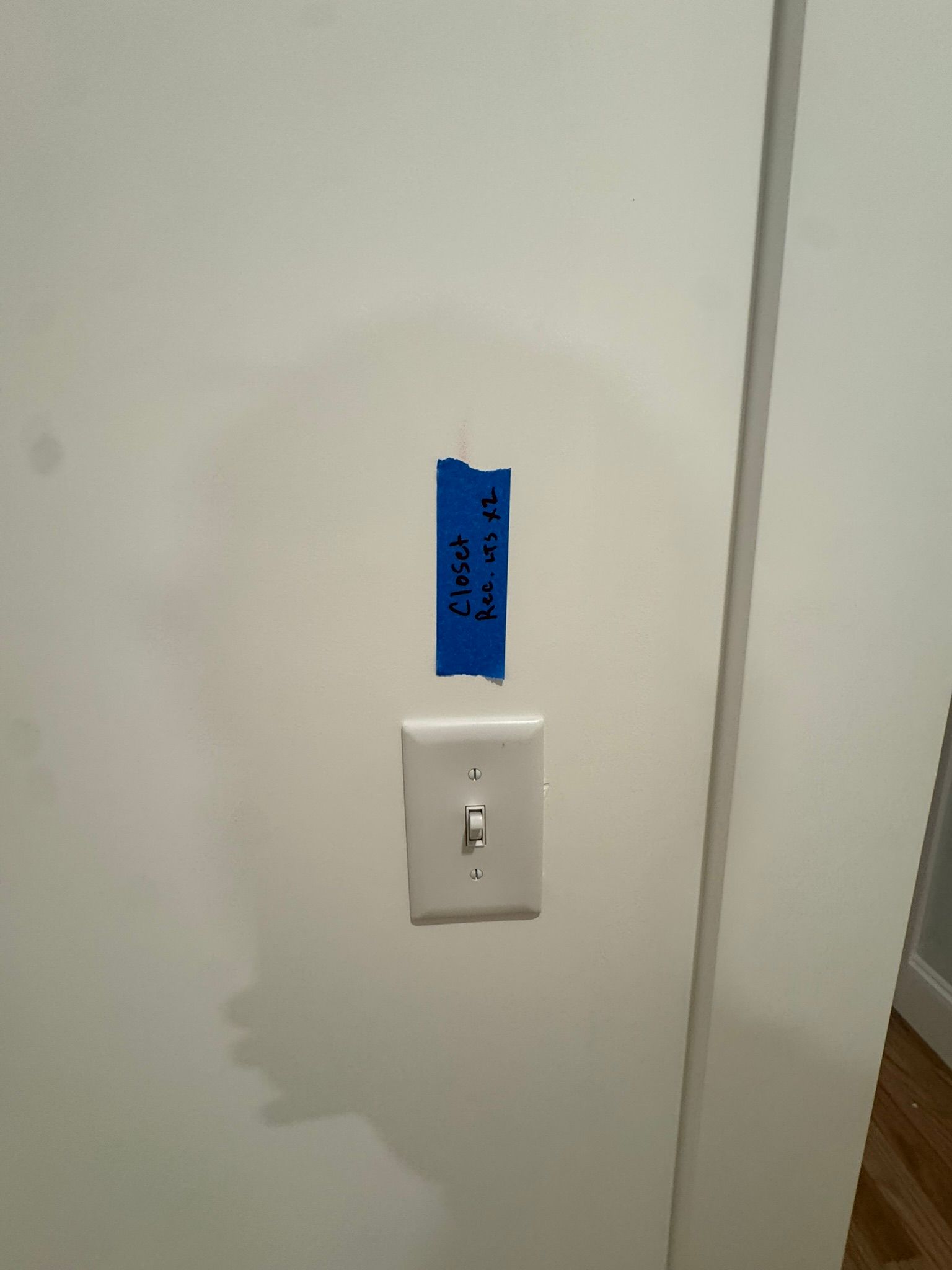 Light switch on a white wall with blue tape label above it