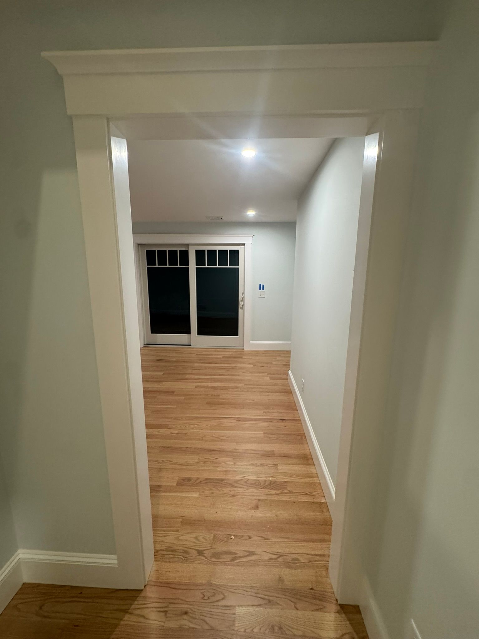 Empty hallway with wood floors and white walls leading to a sliding glass door.