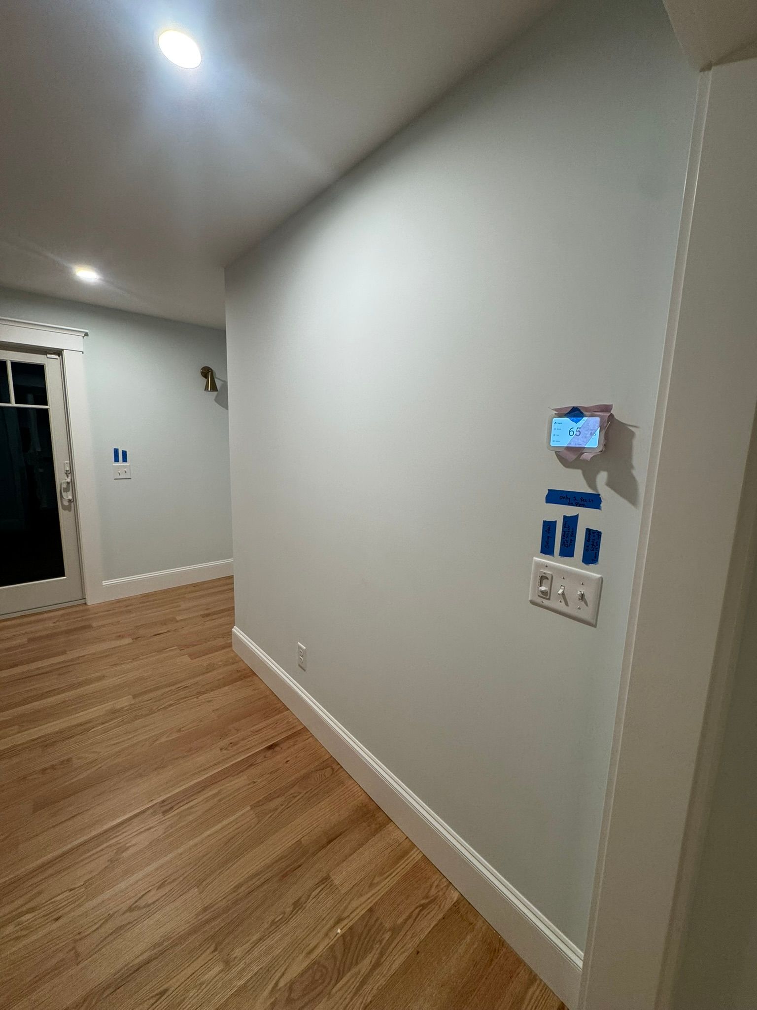 Empty hallway with light wood floor, gray walls, and a wall-mounted thermostat/control panel.