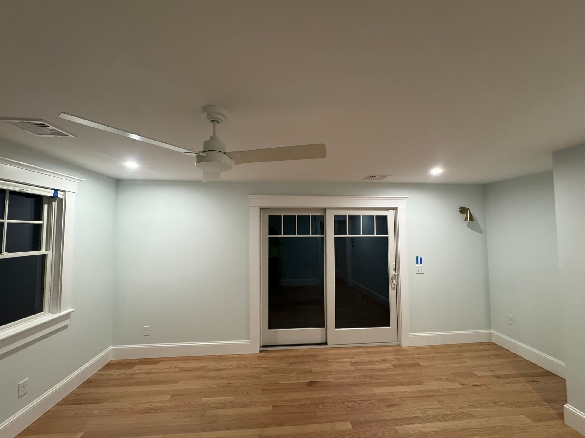 Empty living room with hardwood floors, white walls, ceiling fan, and sliding glass doors.