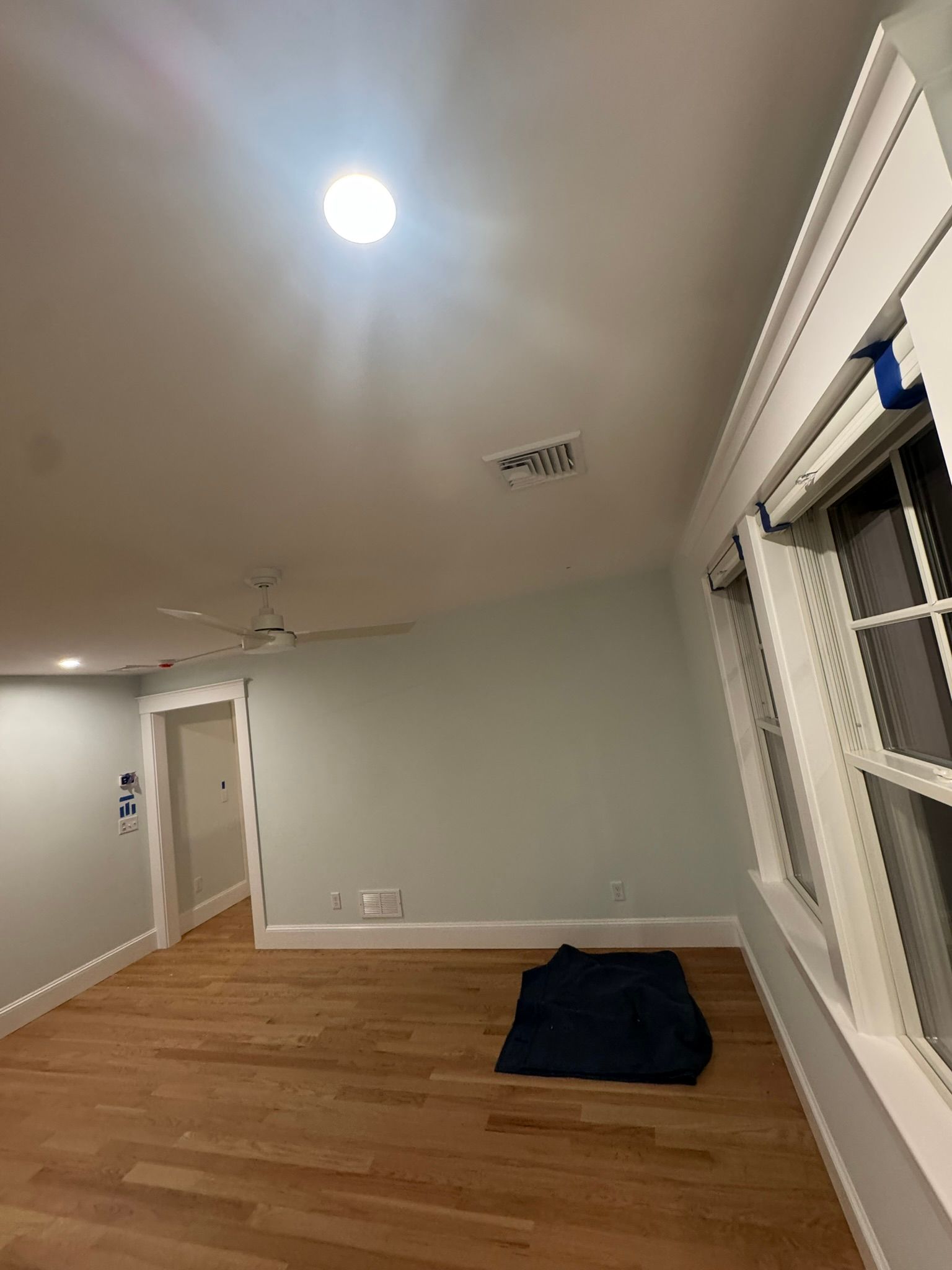 Empty room with hardwood floor, ceiling light, open doorway, and large window with blinds.