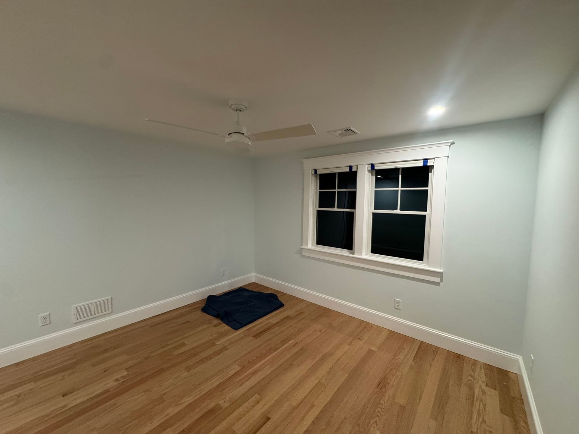 Empty bedroom with light gray walls, hardwood floors, and a window with white trim.