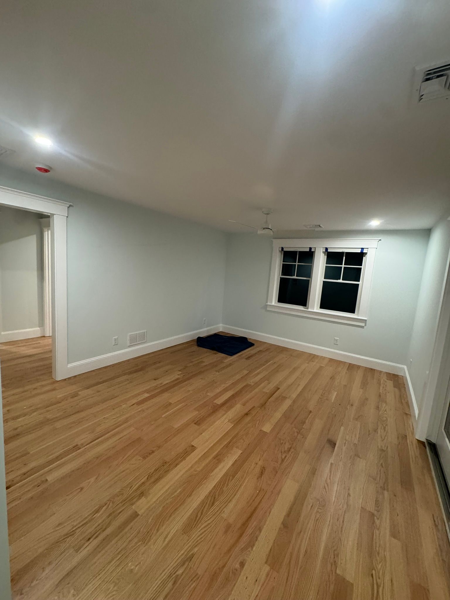 Empty room with light wood floors, white walls, a window, and a doorway leading to another room