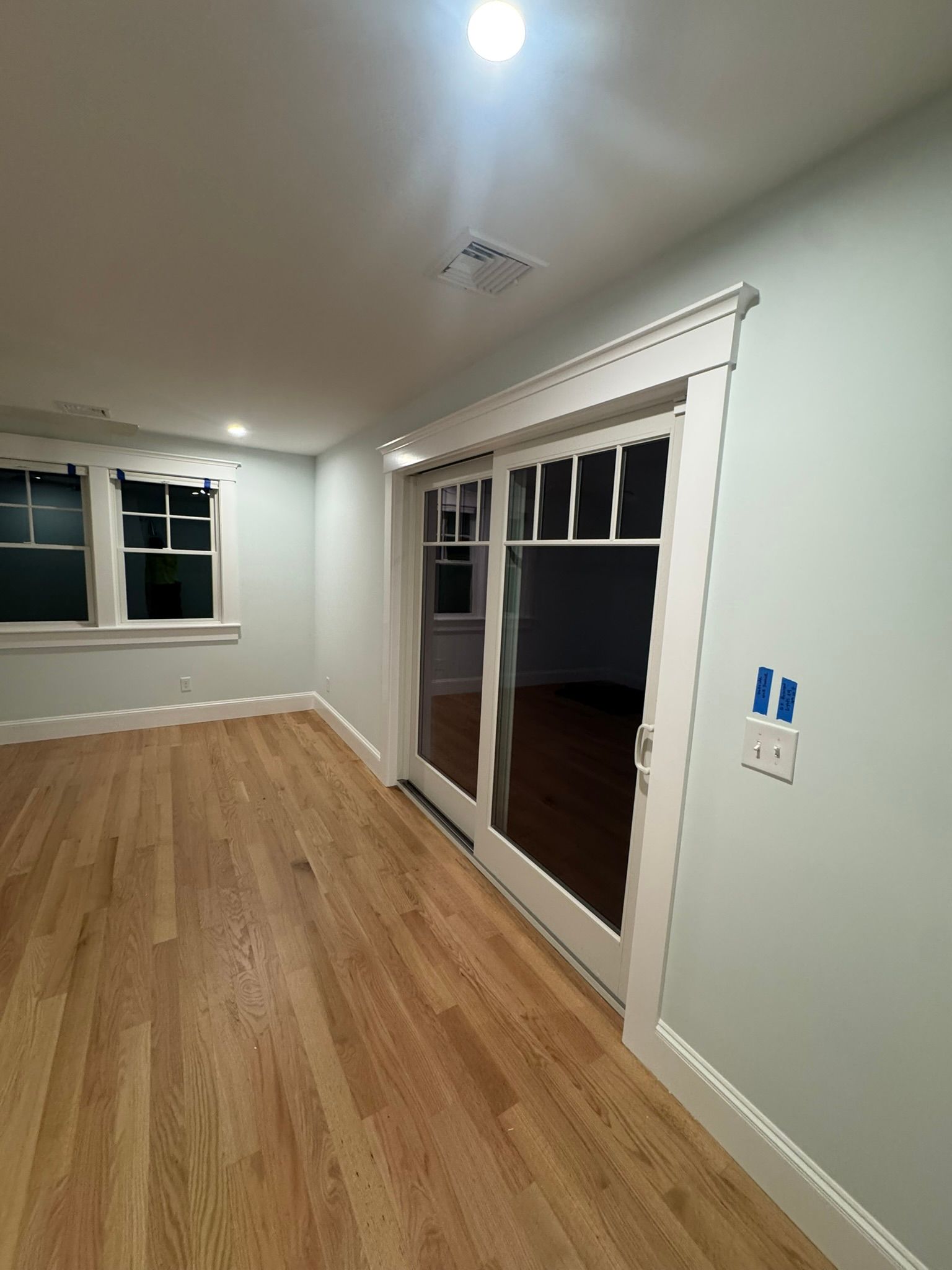 Empty room with hardwood floors, white walls, windows, and a glass door leading outside
