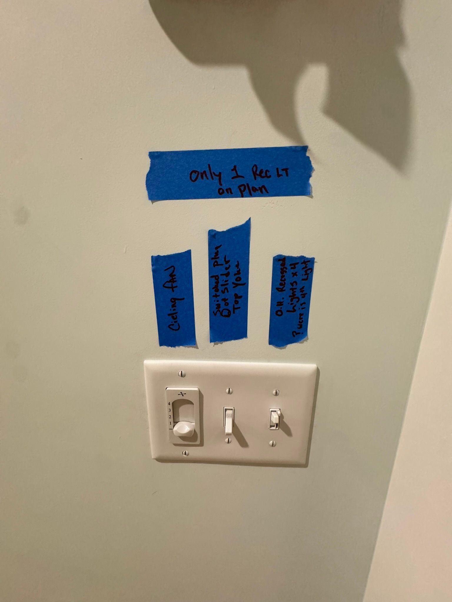 Wall light switch with blue tape labels on a beige wall