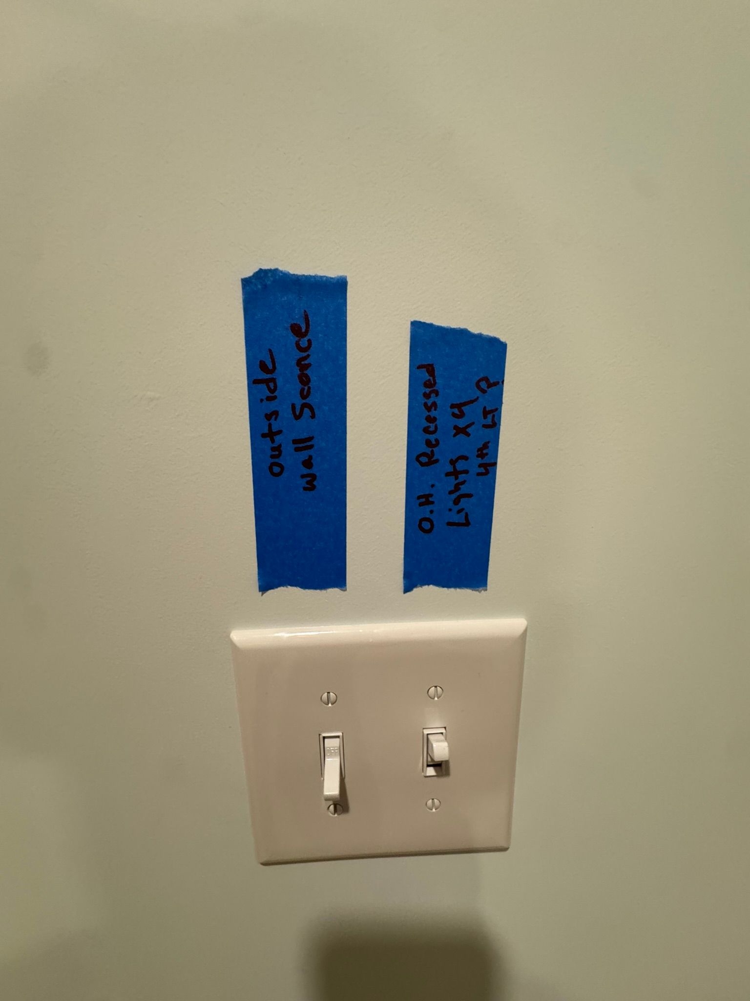Light switch panel with two blue tape labels on a beige wall