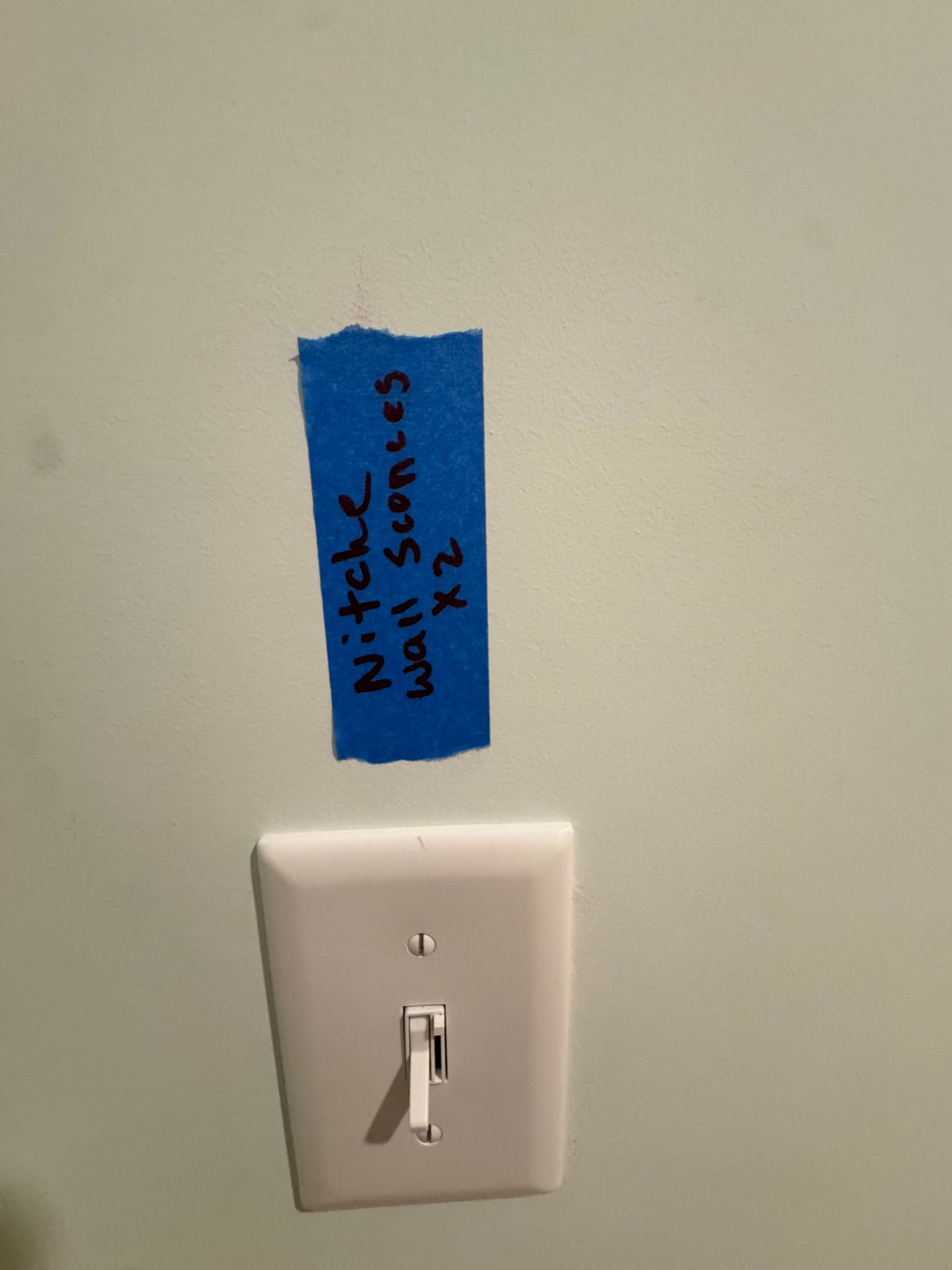 Blue tape label above a white light switch on a beige wall.